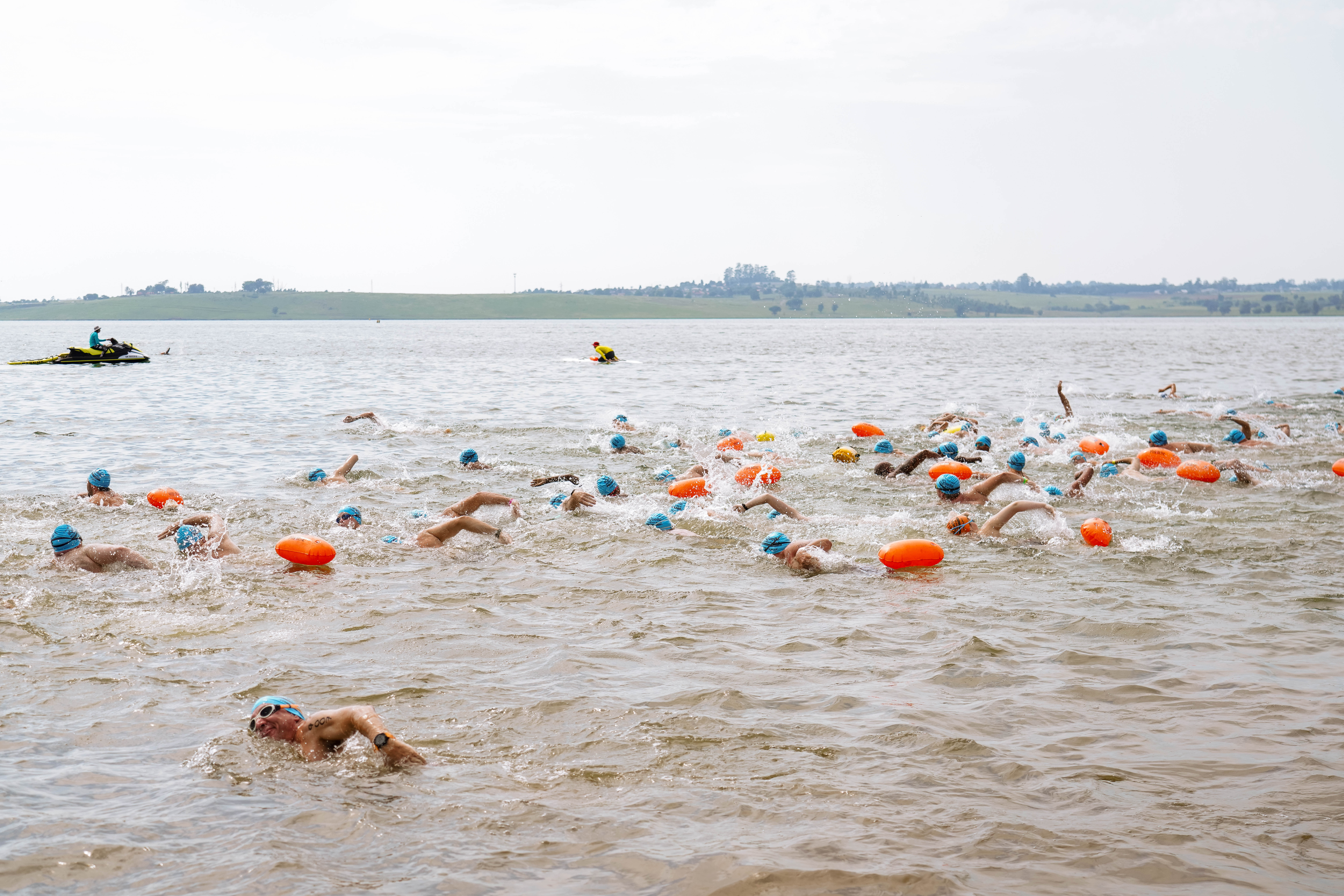 Smiling young swimmer in an orange cap giving a shaka sign beside the start pontoon
