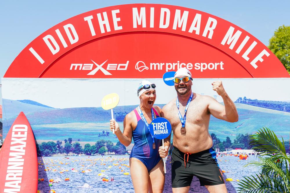 Two finishers with medals and a First Midmar sign at the I Did The Midmar Mile wall
