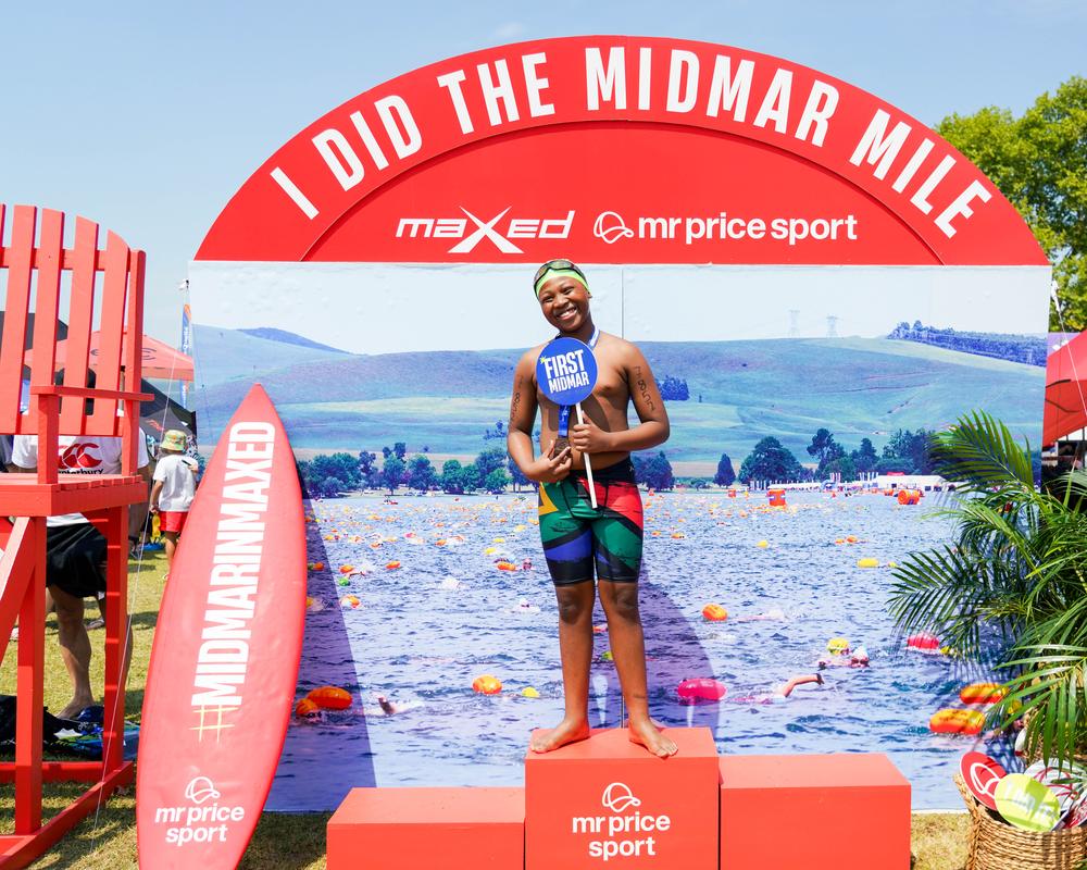 Young swimmer in a South African flag costume holding a First Midmar sign