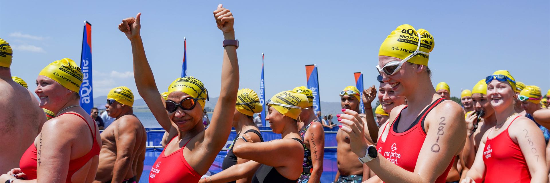 Team MRP Sport swimmers in red costumes and yellow Midmar caps cheering at the start.